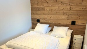 A neatly made bed with white bedding in a room with wooden panel walls and a white floor.