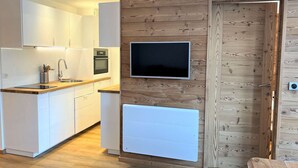A modern kitchen with white cabinetry, a built-in oven, a microwave, and a flat-screen TV mounted on a wooden wall.