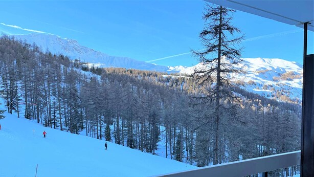 A snowy mountain landscape with a clear sky, a forested area, and a person skiing.