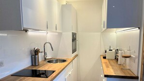A compact kitchen with white cabinetry, a wooden countertop, a stainless steel sink, and a built-in oven.