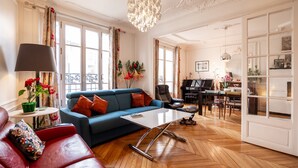 A spacious living room with a blue sofa, a red sofa, a white coffee table, and a piano in the background. - Vivid, Vivace, by Veeve (Paris)
