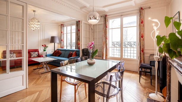 A spacious living room with a glass-top dining table, a red sofa, a blue sofa, and a fireplace. - Vivid, Vivace, by Veeve (Paris)