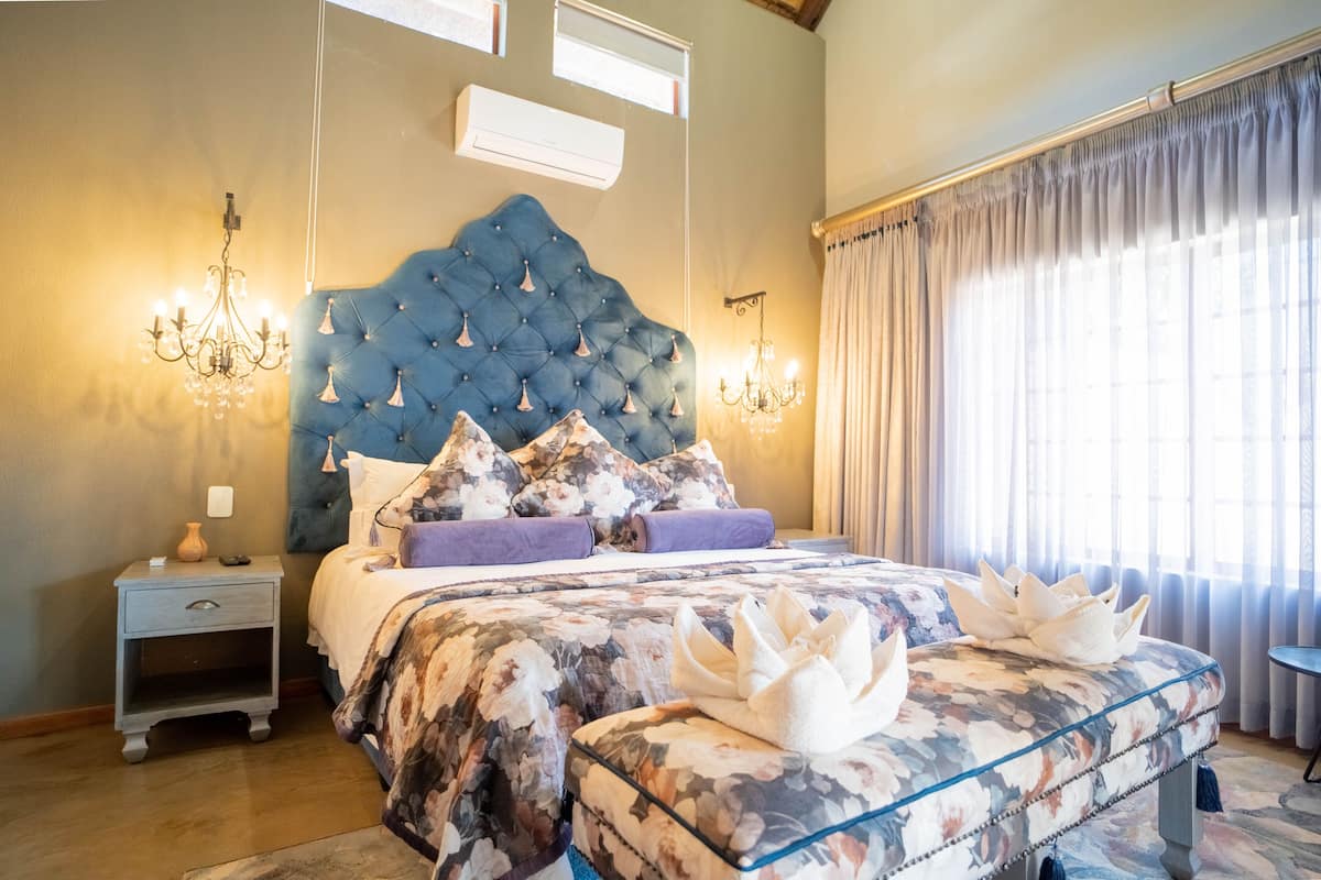 A bedroom with a tufted headboard, floral bedding, a glass bedside table, and a chandelier.