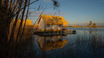 Una casetta galleggiante con tetto giallo su un lago tranquillo, circondata da canneti e alberi.
