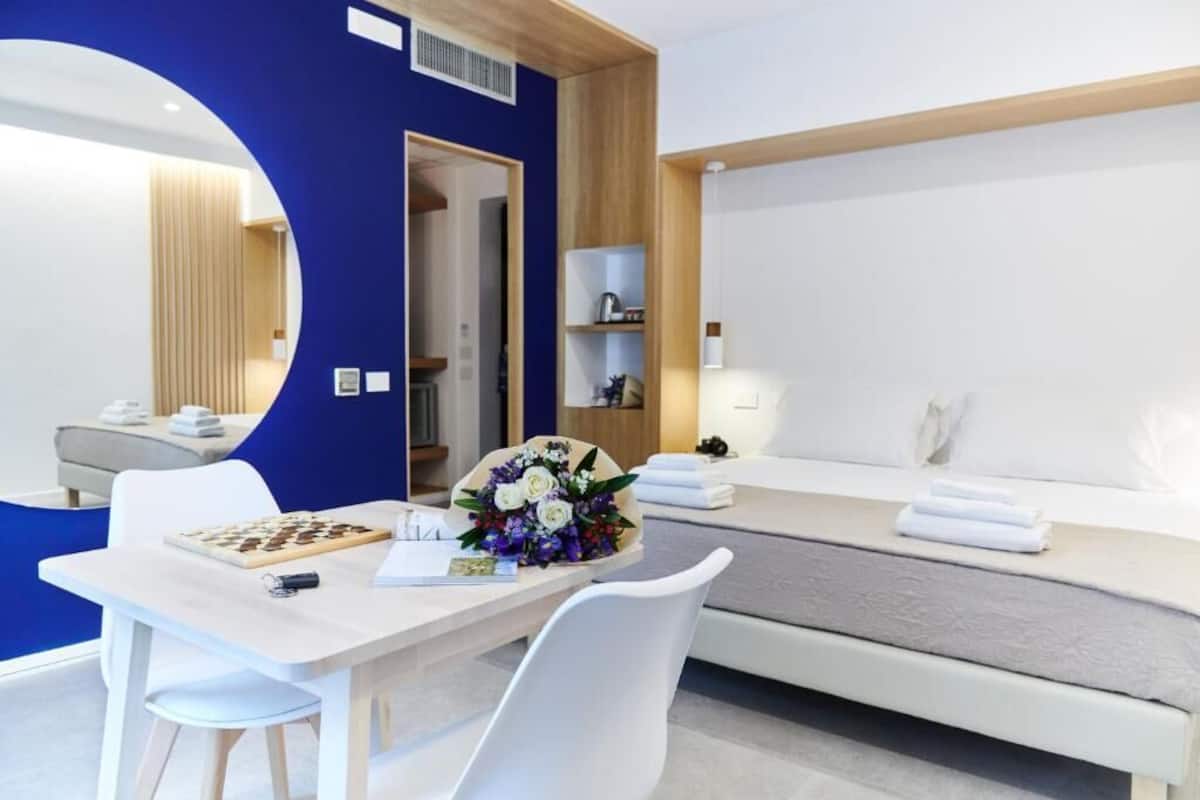 Une chambre d’hôtel moderne avec un bureau blanc, un jeu d’échecs, un bouquet de fleurs et un lit parfaitement fait.