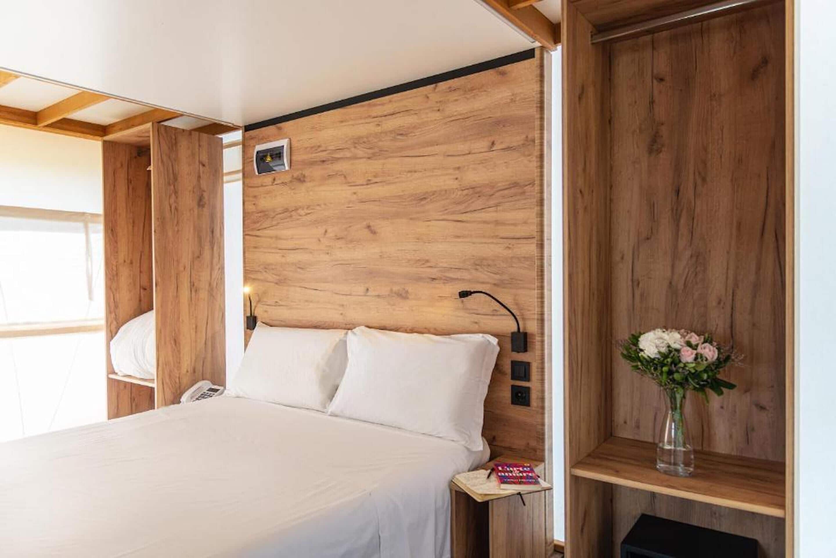 Un dormitorio con cabecera de madera, una mesita de noche con un teléfono y una pequeña estantería con un florero.