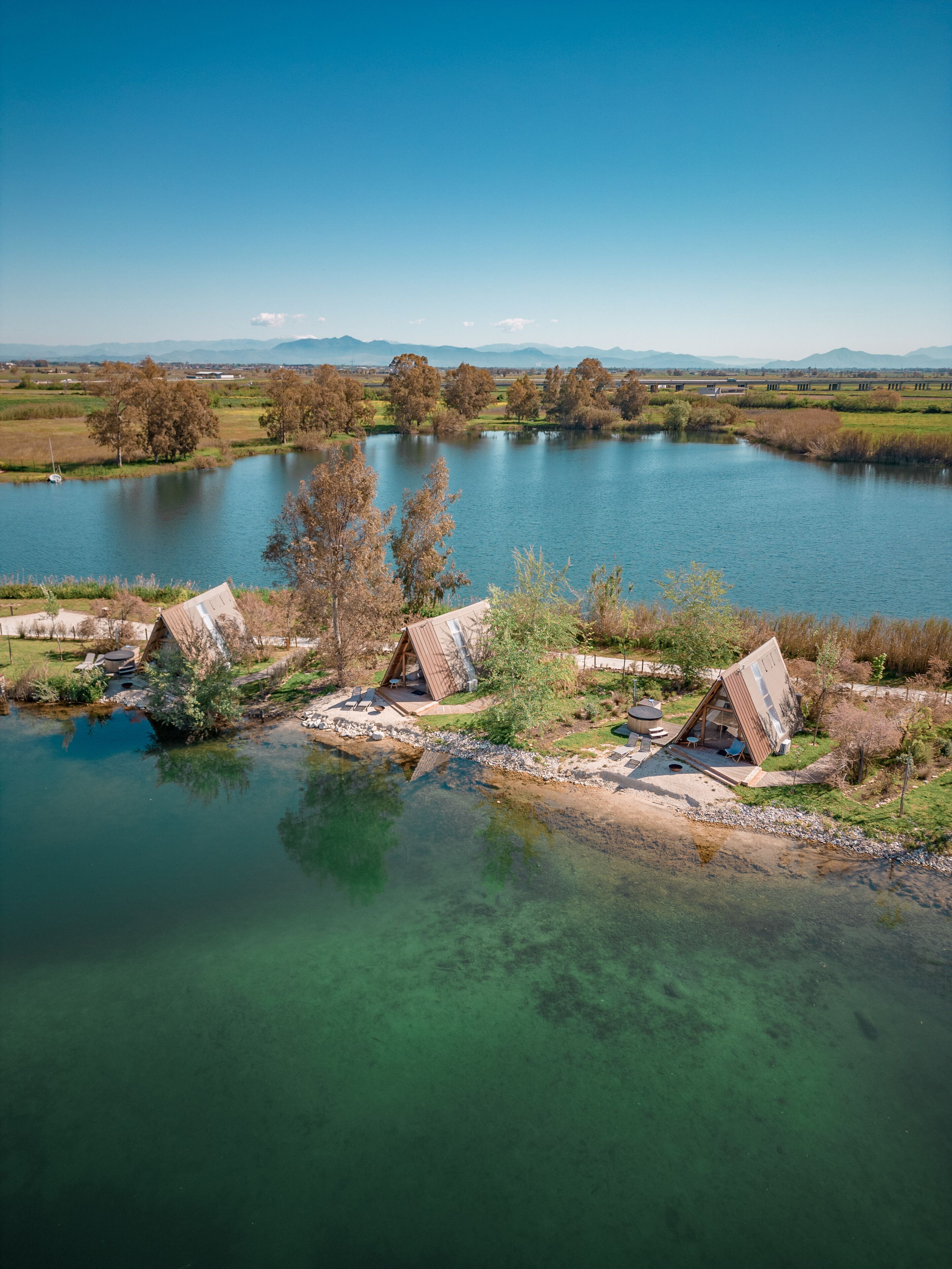 Une propriété au bord du lac comprenant trois chalets rustiques, une eau cristalline et une chaîne de montagnes visible au loin.