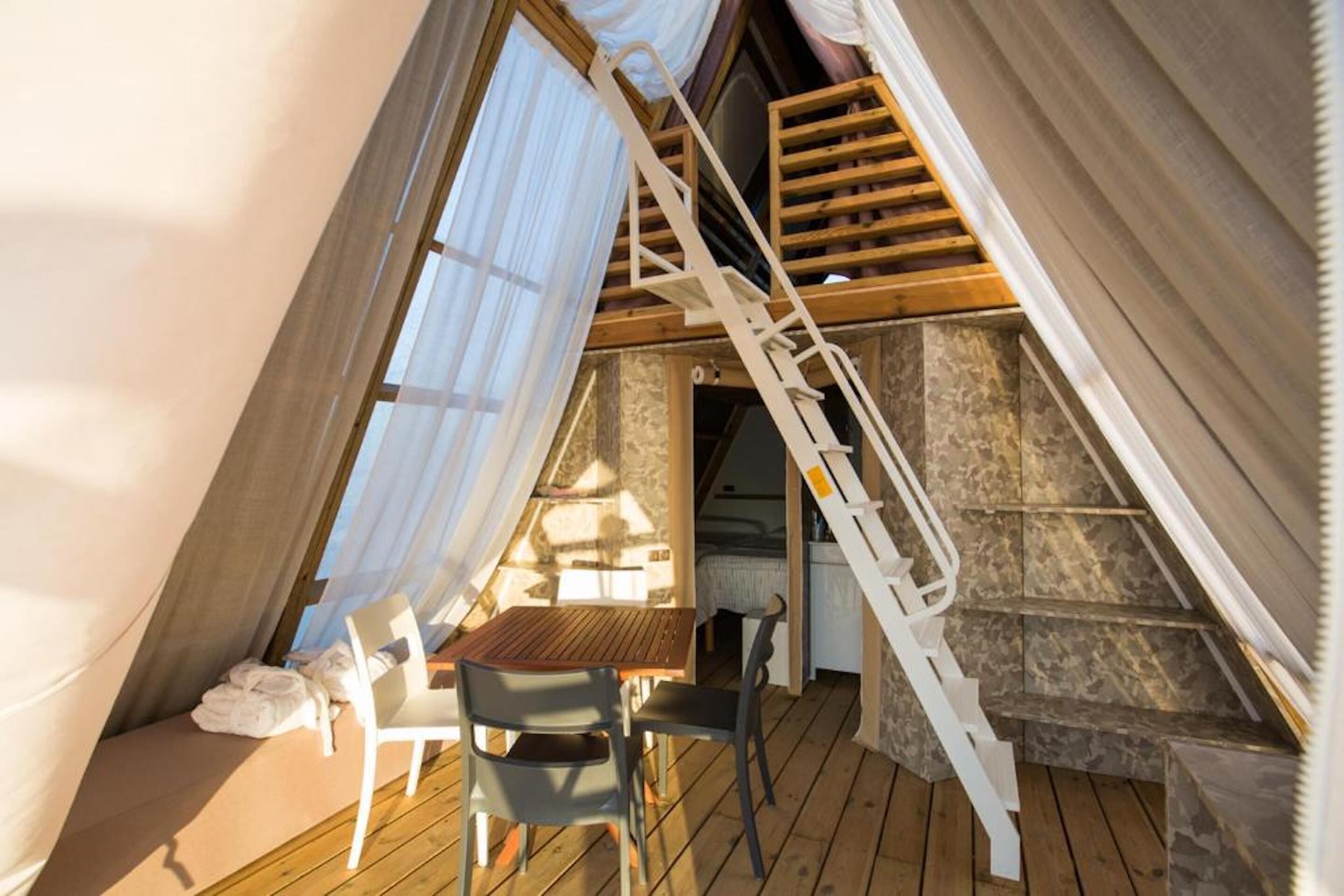 Una camera da letto mansardata accogliente con una scala in legno, un tavolino e una sedia.