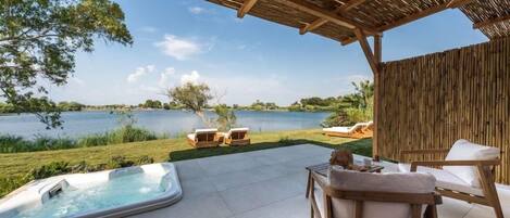 Un espacio al aire libre techado con un jacuzzi, sillones de descanso y vistas a un lago.