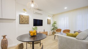 Una sala de estar moderna con una mesa de comedor redonda, un sofá y un televisor montado en la pared.