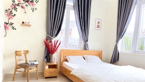 A bedroom with a wooden bed, a nightstand, a chair, a vase with red flowers, and a wall with a floral design. - Mon Bac Home (Lam Vien - Da Lat)