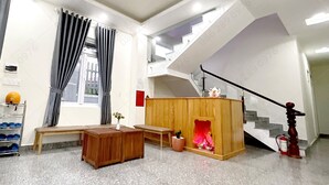 A spacious living area with a wooden bench, a small table with a vase, a fireplace, and a staircase with a railing. - Mon Bac Home (Lam Vien - Da Lat)