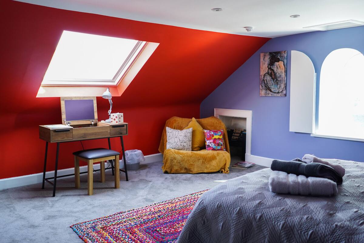 A bedroom with a skylight, a desk, a chair, a bed, and a colorful rug.