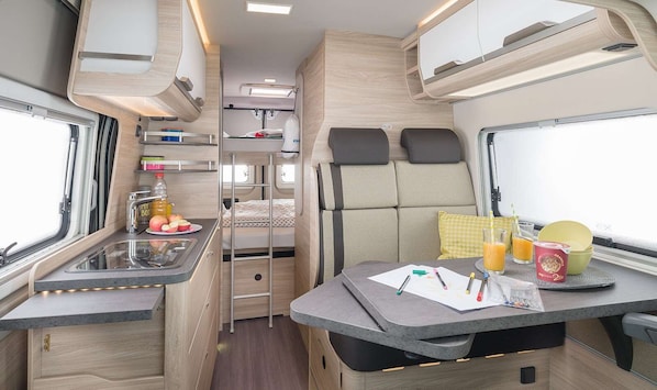 Cozy motorhome interior with a kitchenette, dining area, and sleeping quarters.