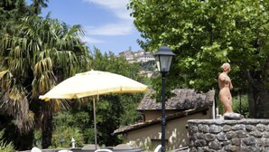 An outdoor patio with a yellow umbrella, stone walls, and a statue. - Vacation home Virgo by Interhome (Cortona)