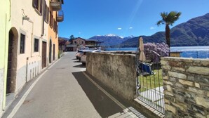 A narrow street with buildings on one side and a lake with mountains in the background. - La tana del pescatore by Interhome (Tremezzina)