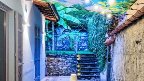 An outdoor dining area with a table and chairs, a string of lights, and a mural of a blue sky and greenery on the ceiling. - La tana del pescatore by Interhome (Tremezzina)