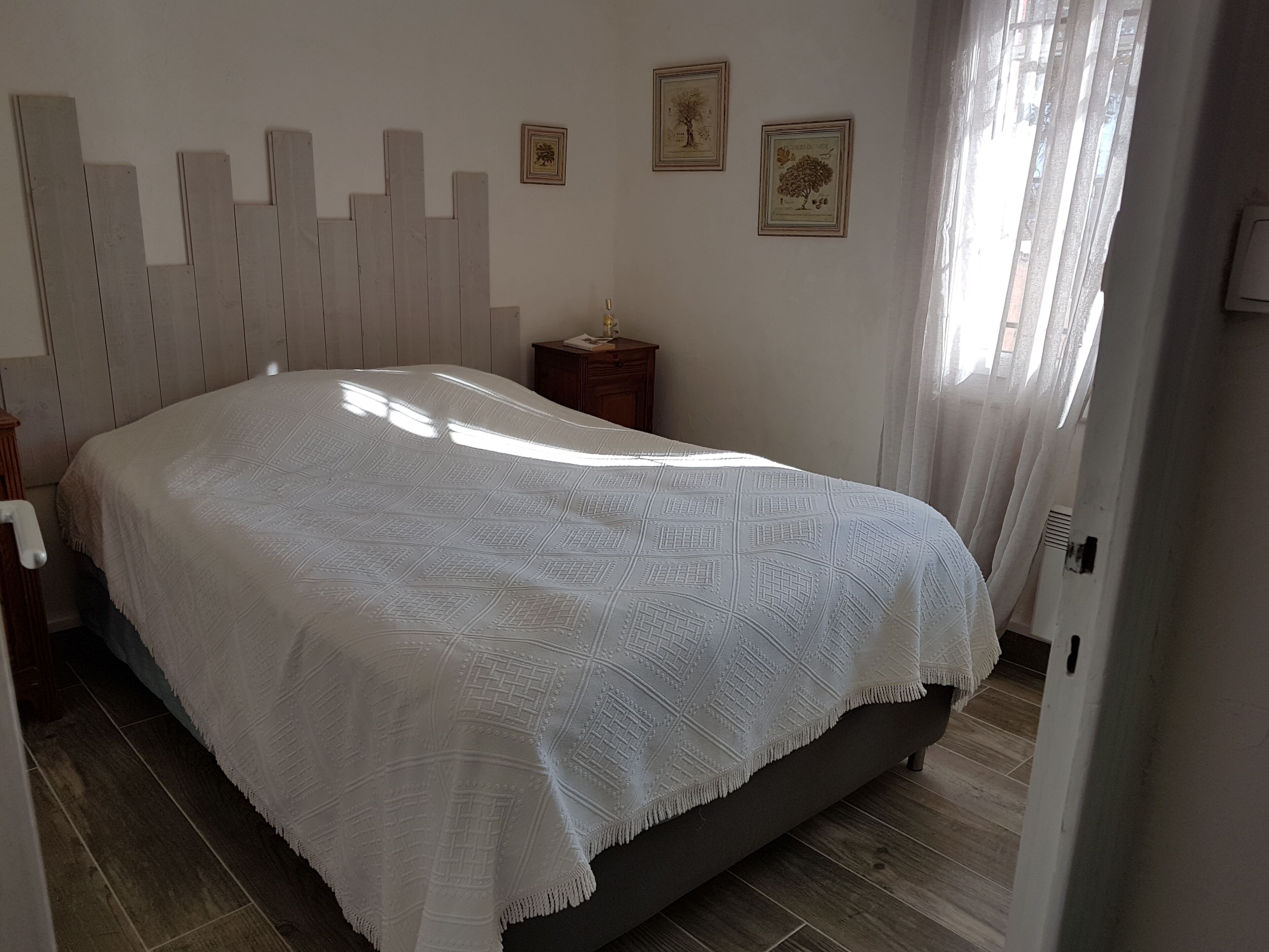 Quarto com uma cama grande, cabeceira de madeira, mesa de cabeceira e duas fotos emolduradas na parede.