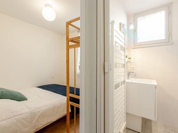 Una habitación pequeña y luminosa con una cama litera, un lavamanos blanco y una ventana.