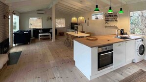 A spacious living area with a large island, wooden flooring, and a kitchen with a washing machine. - Newly renovated summer house in Hornbæk, close to water and city (Hornbæk)