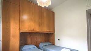 Une chambre avec deux lits simples, une armoire en bois et un luminaire suspendu.