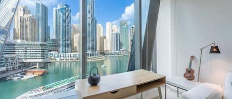 A modern hotel room with a large window offering a view of a city skyline and a marina.