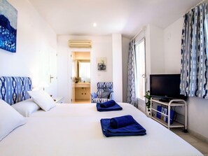 A hotel room with a bed, a TV, a desk, and a bathroom visible through an open door.