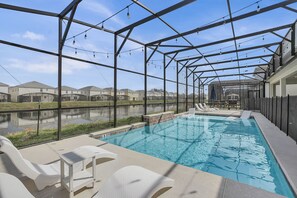 A swimming pool with lounge chairs, a covered area with a metal frame, and a view of residential buildings.