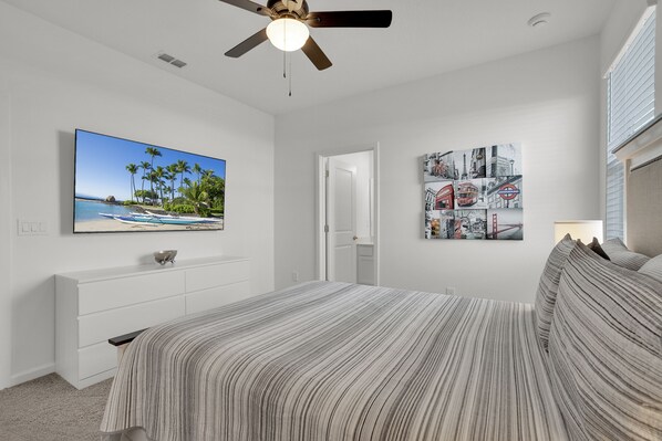 A bedroom with a bed, a ceiling fan, a TV on the wall, and a door leading to another room.