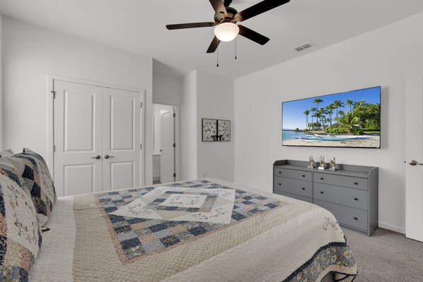 A bedroom with a bed, a ceiling fan, a dresser, and a painting of a beach scene.