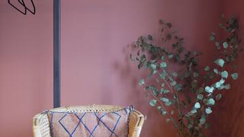 A wicker chair with a patterned cushion, a vase with green foliage, and a vertical black object on the wall.