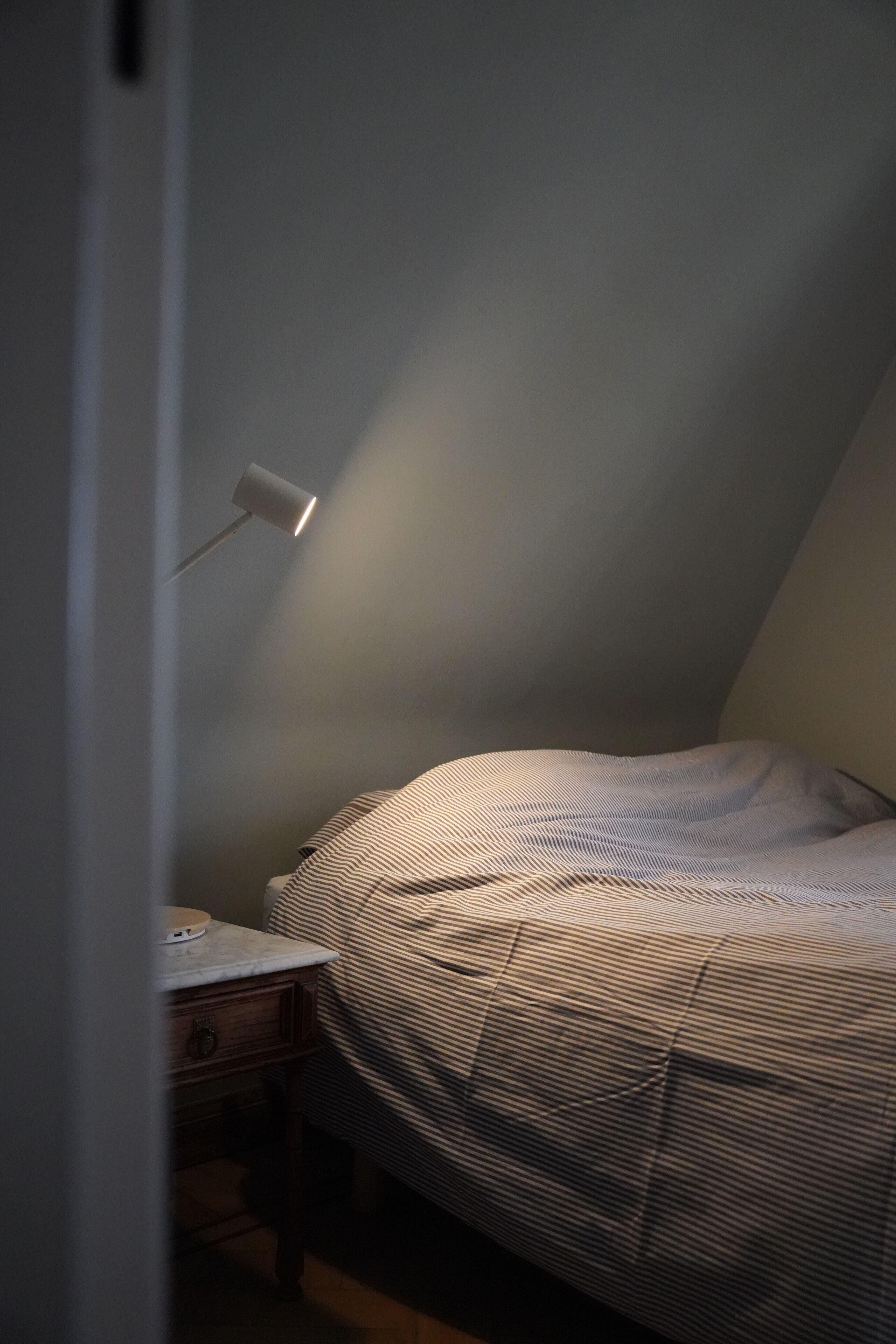 Une chambre avec un plafond en pente, une table de chevet avec une lampe et un lit avec une literie à rayures.