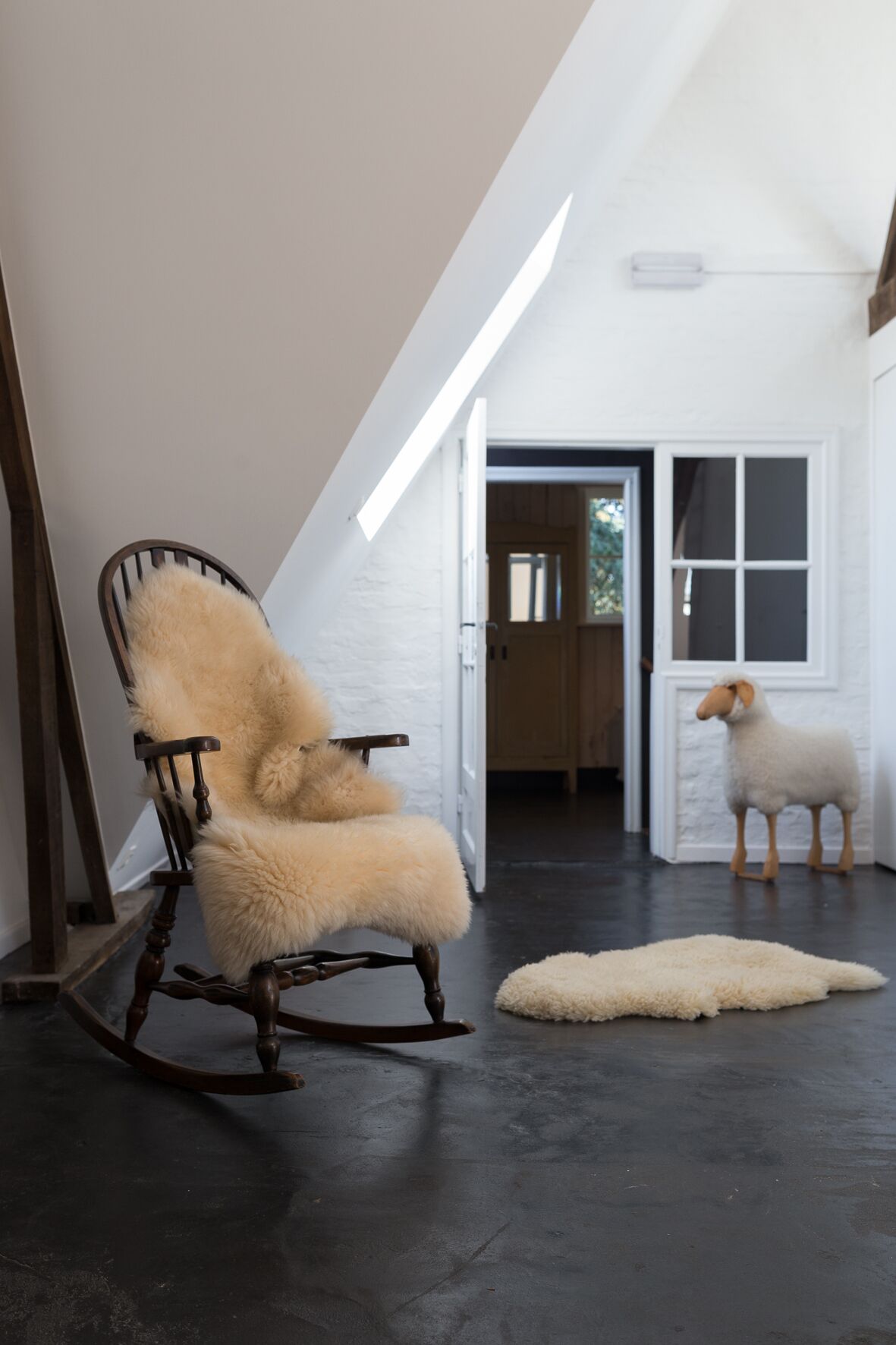 A room with a rocking chair, a fluffy rug, and a wooden sheep figure.