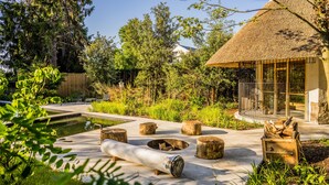 Ein Haus mit Strohdach und Glasveranda, umgeben von einem Garten mit Teich und Holzmöbeln.