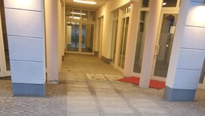 Un pasillo con suelo de baldosas que conduce a una entrada con puerta de vidrio.