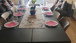 Un comedor con una mesa dispuesta para cuatro, vistas al exterior a través de un ventanal grande, y un rincón de estar acogedor con un sofá y sillones.