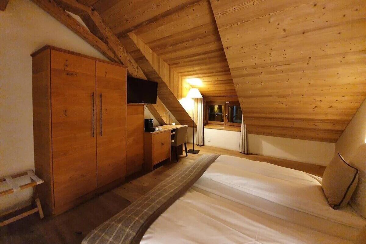 Ein gemütliches Schlafzimmer im Dachgeschoss mit Holzbalkendecke, einem Bett, einem Schreibtisch mit Stuhl und einem an der Wand befestigten Fernseher.