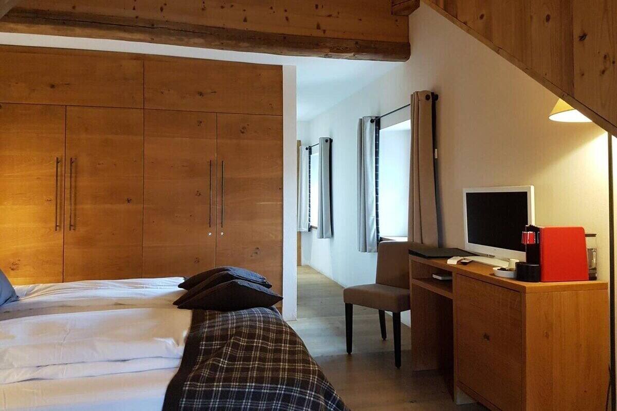 Ein Hotelzimmer mit Holzboden, einem Bett mit weißer Bettwäsche, einem Schreibtisch mit Computer und einem Fernseher.