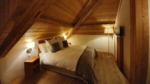 A cozy attic bedroom with a wooden ceiling, a bed with pillows, a nightstand, a lamp, and a TV. - Auberge de l'Union Arzier (Arzier)