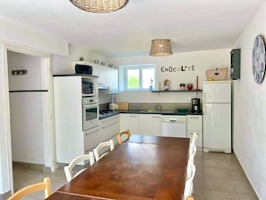 Une cuisine avec des meubles blancs, une table à manger en bois et une horloge au mur.