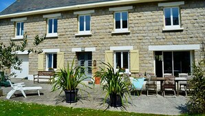 Un bâtiment en pierre doté de nombreuses fenêtres, d’une terrasse et de plantes en pot.