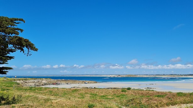 Un paysage côtier caractérisé par un ciel dégagé, une plage de sable et des affleurements rocheux.