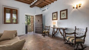 Ein Zimmer mit Holzboden, einem beigen Sofa, zwei Holzstühlen, einem kleinen Tisch und einer zur Außenwelt führenden Tür.