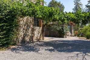 A stone building with a gravel driveway, surrounded by greenery and trees.