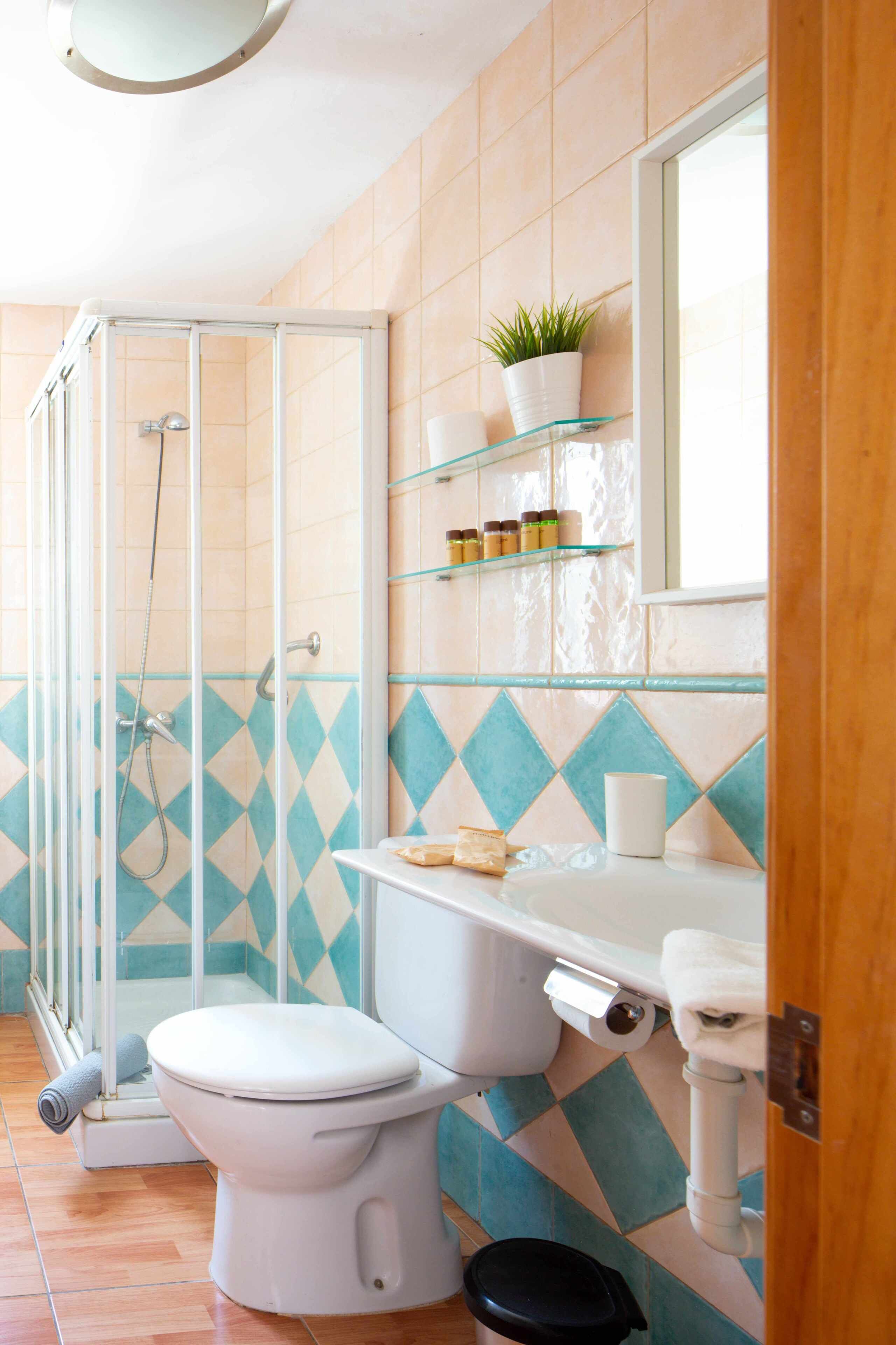 Un baño con cabina de ducha de vidrio, inodoro, lavabo con espejo y repisa con artículos de aseo.
