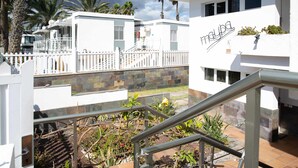 A multi-level building with a white exterior, a balcony with a white fence, and a staircase with metal railings. - Apartamento Maypa 1 Calma (Maspalomas)