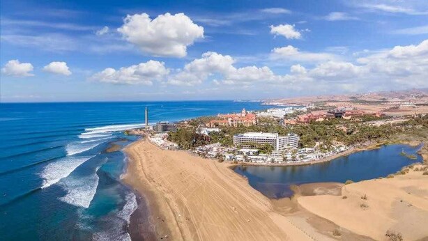 A coastal resort with a beach, a large body of water, and a central building with multiple floors. - Apartamento Maypa 1 Calma (Maspalomas)