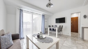 Una sala de estar moderna con comedor, un televisor de pantalla plana montado en la pared y una escalera que sube a otro nivel.