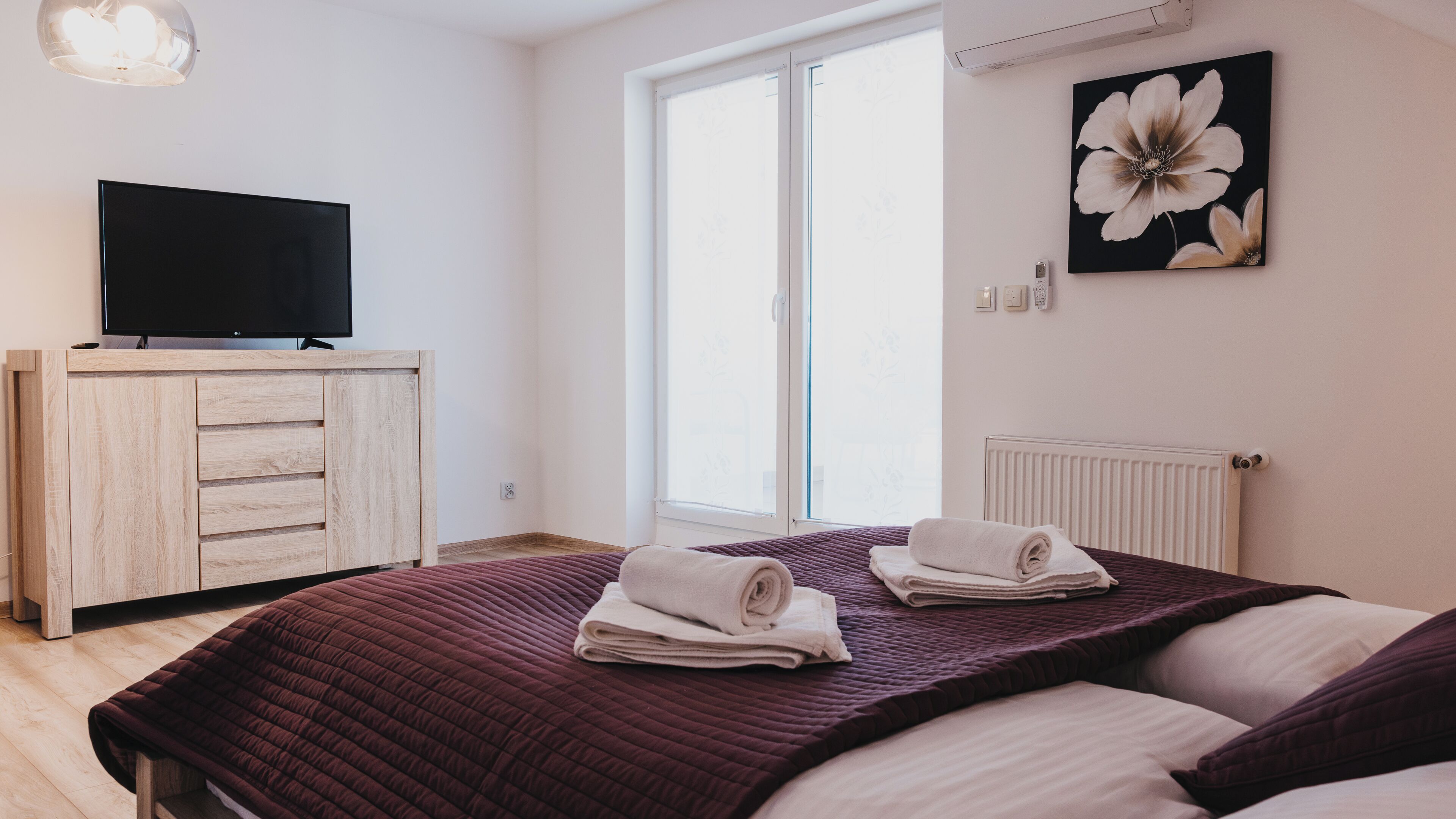 A bedroom with a bed, a TV, a radiator, and a window.