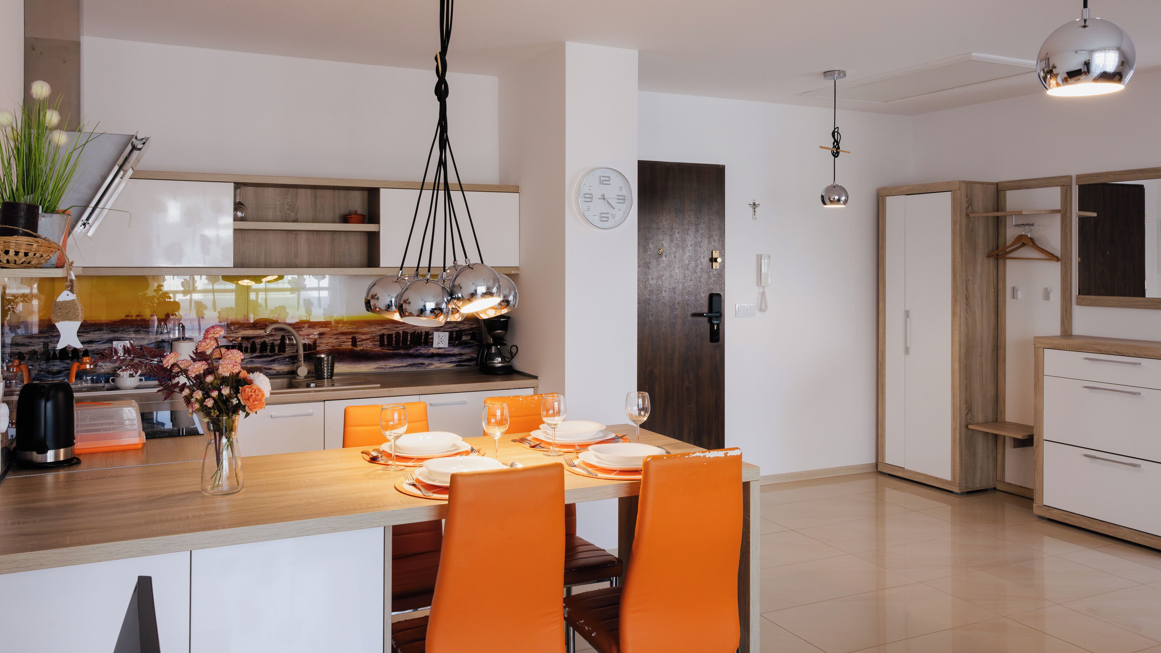 Eine moderne Küche mit Essbereich, mit einem Holztisch, orangefarbenen Stühlen und einer hängenden Pendelleuchte.